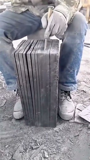 Stonemason Wearing Work Gloves and Jeans Using a Chisel and Hammer to Split a Stack of Slabs