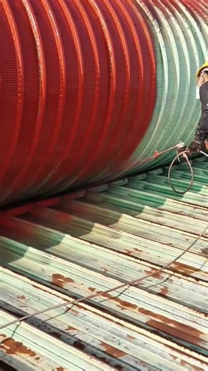 Spraying red paint onto a curved industrial metal roof surface using professional high pressure tool