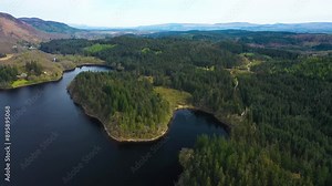 Green pine tree forest in the Trossachs National Park. Clear day on Loch Ard with rolling wooded hills. Beautiful wild landscape. Scottish Highlands, Scotland, United Kingdom.
