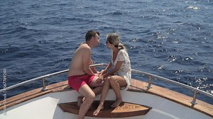 Smiling romantic couple sitting and talking on yacht deck, honeymoon love concept