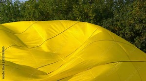 Slow motion yellow balloon envelope sail inflating for the flight. Trees in background.