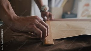 Close up of hands of anonymous seamster using pattern to draw on garment while working in dressing studio