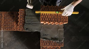 Close-up of Builder using leveler for brickwork. Stock footage. Professional work of builders during brick laying. Builder corrects bricks during masonry with level and tapping with hammer