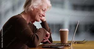 Slowmo of cheerful mature woman in outdoor setting scrolling through website on computer laughing. Attractive senior woman watching something on laptop smiling. 4k