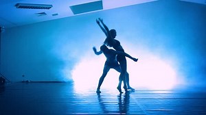 Couple practicing the elements of dance against a black background in the beam of a spotlight