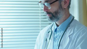Experienced doctor talking with patient and taking notes on clipboard during medical consultation in hospital ward. Tilt-down shot