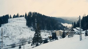 People moving up snow mountains on ski elevator. Beautiful snowy forest landscape with houses and fir trees covered with snow. Winter holiday and recreation, editorial video
