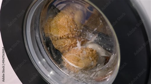 Washing machine cleaning a teddy bear with detergent. Washing machine spinning with a teddy bear and other clothes inside, with soap bubbles and detergent cleaning the stuffed animal