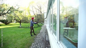 Woman washing conservatory window with water jet reflecting on glass. Focus.