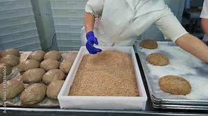Women roll fresh loaves of bread in breading crumbs before baking. Working of modern bakery. Food production industry