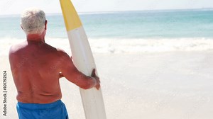 Old retired man going to the beach while holding surfboard Stock Video