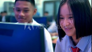 Asian female and male high school students in white uniform are enjoying social media in computer classroom.
