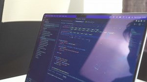 Premium stock video - Side view of computer code scrolling back and forth on a reflective laptop computer screen with retina display technology