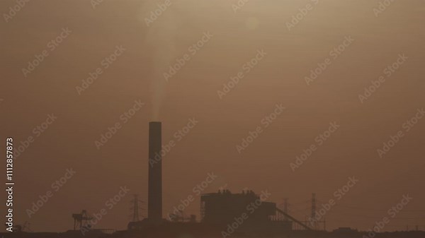 Smokestack emits smoke from power plant, silhouetted against sunset sky. This industrial skyline shows the environmental impact of fossil fuel for air pollution, carbon emissions, and climate change.