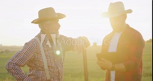 Full length view of the senior farmer engineer coaching young intern farming technologies. Mature specialist telling something to his colleague. Off season harvest and agronomy concept