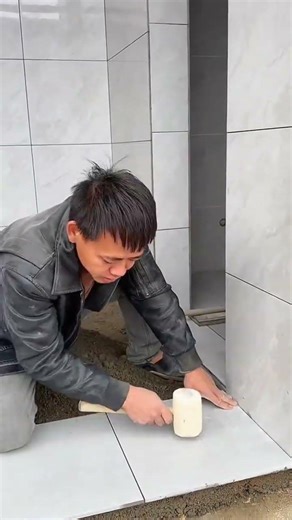Tapping ceramic floor tile firmly with rubber mallet