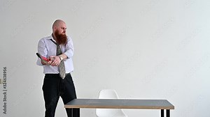 Angry bald man with a red beard in the office in a business suit smashes an ax with a computer. The manager with a nervous breakdown, breaks the monitor.