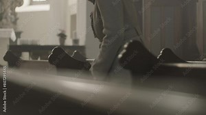 Religious woman crossing herself and sitting on pew bench in Christian church side view medium shot. Mid adult caucasian person kneeling and praying in cathedral Stock Video