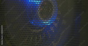 Computer cooling fans illuminated by blue led lights spinning behind black wire mesh macro close up shot shallow depth of field