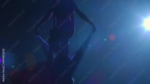 Silhouette of aerial circus gymnast performing on aerial silk and waving canvas like wings. Beautiful circus show performed by young woman acrobat on black background with blue backlight. Slow motion.