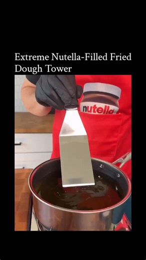 Learnbit.io on Instagram: "The video showcases an outrageously indulgent Italian dessert preparation featuring massive amounts of Nutella. A chef wearing a red Nutella-branded apron and black gloves starts by scooping pale dough from a container and frying rectangular pieces in hot oil until golden and crispy. He then stacks three fried dough pieces on a plate, generously filling the layers by squeezing thick streams of Nutella from large food-service pouches between each one, creating oozing ch
