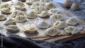 Pelmeni dumplings making process: Woman's hand taking raw, unccoked, pelmeni stuffed with meat filling. Gluten free recipe for traditional Russian cuisine. Floured wooden surface, handmade dumplings.