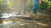Kid walks barefoot in the forest creek with her parent. Family hike...