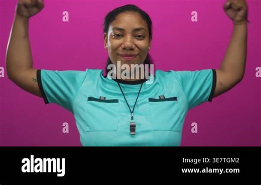 Referee woman flexes biceps while holding whistle in magenta studio setting showcasing refereeing gear; empowerment strength Stock Video Footage - Alamy