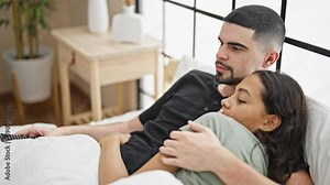 Beautiful couple in love, lying together on the comfy bed in their bedroom, watching an intense movie while cuddling late at night in their cozy apartment