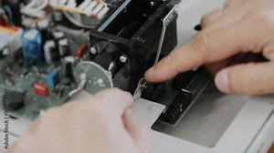 An engineer or technician attaches a cable to a computer board. An engineer assembles the device by hand. Demonstrate technical skills and electronics maintenance.