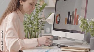 Professional female marketing specialist analyzing charts and diagrams on desktop computer in office, attaching sticker note with reminder on monitor
