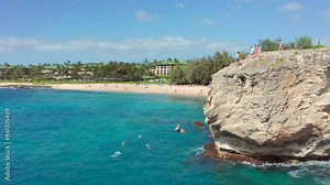 People jumping off cliff in Hawaii. Friends jumping from high rock into hawaiian ocean. Summer fun lifestyle slow motion aerial drone shot
