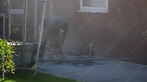 Construction worker wearing dust mask is cutting concrete slabs of pavement with circular saw outdoors.