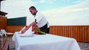 Cook at home, Professional chef serves a table on the terrace, a table covered with a white tablecloth and napkins, forks, plates knives are on the table, food in the open air