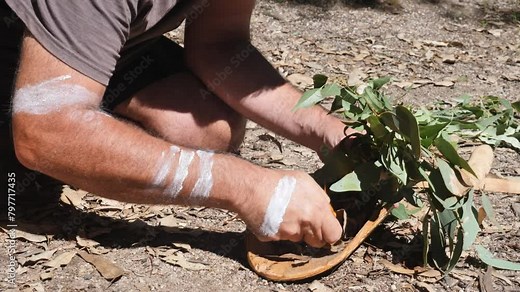 Australian Aboriginal Smoking Ceremony, man creates smoke from burning leaves on a traditional wooden bowl as part of an ancient indigenous custom.