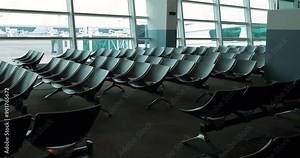Empty chairs in tranquil airport lounge at international terminal. Camera begins with close-up of seating area and then quickly zooms out to reveal wide-angle view of deserted boarding gate waiting