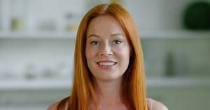 Portrait of young beautiful woman standing in kitchen, smiling, looking at camera, looking confident in future, enjoying life, long red straight hair, grey eyes, freckles, Caucasian. 4K, RED camera.