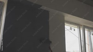 Painting walls with dark paint in new room with unfinished renovation. Finishing process of fresh room with paint using roller slow motion