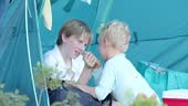 Two boys sit inside a camping tent, enjoying a moment together in...