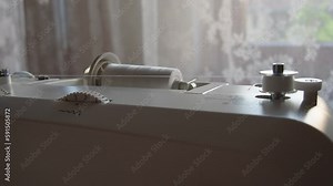 Winding white thread on a bobbin. Using an electric foot sewing machine at home. Sewing preparation. Automatic winding of threads. Tailoring and decor items.