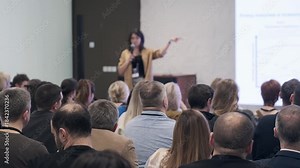 Presenter speaks to crowded room during training session audience listens notes focus leadership communication industry insights in dynamic conference setting. Stock Video