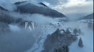 Aerial drone view of foggy Town in dolomites in Italty. Italian mountain town Berguzzo in alps. Adamello Brenta park in dolomites Trentino. Cloudy winter day in small town in the Italian mountains.