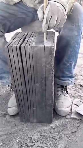 splitting a large solid block into several thin slate pieces manually with a metal chisel and hammer