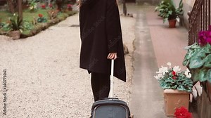 Back view of tourist woman in black. Close-up view of female legs walking with a suitcase in the street.