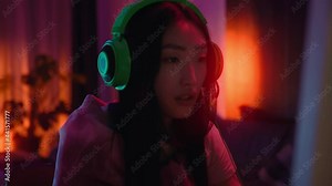 Young asian woman with headphones gamer playing in online video game. Cyber, microphone, live stream, entertainment, gaming, neon, player, enjoy, videogame. Slow motion