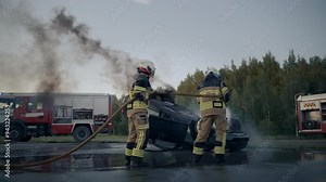 Firefighters Extinguish a Burning Car that was Involved in a Traffic Accident During the Day. Smoke Billows as Emergency Vehicles and First Responders Ensure Safety and Control at the Spot