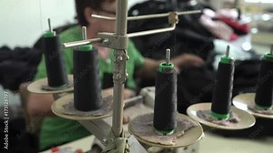 Sewing machine pulling threads of spools in focus, professional female tailor working in the blurred background, steadicam shot to the mature woman, close up, room interior, shallow depth of field