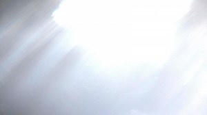 The bride in a wedding dress runs and smiles at the camera. The sun's rays of backlight illuminate the camera with flashes. The bride runs between the rocks