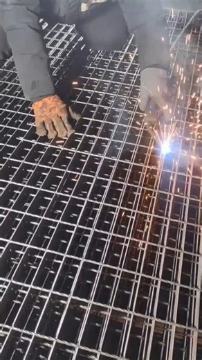 A worker is welding steel wire mesh panels together with bright sparks flying