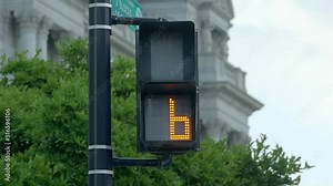 Modern LED street light walk signal counting down for pedestrian crosswalk on corner to allow people on foot to traverse a busy intersection of roads with cars at a stop light